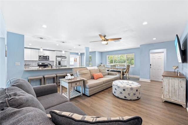 living area with recessed lighting, visible vents, light wood-style floors, a ceiling fan, and baseboards