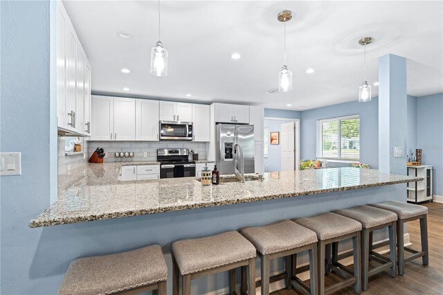 kitchen with stainless steel appliances, a peninsula, decorative light fixtures, and white cabinets