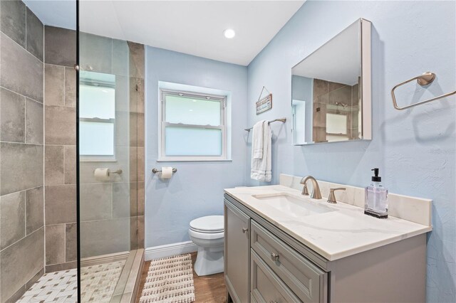 bathroom featuring a walk in shower, toilet, wood finished floors, vanity, and baseboards