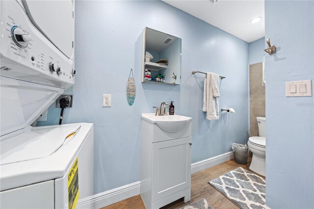 bathroom featuring toilet, stacked washer and dryer, wood finished floors, vanity, and baseboards