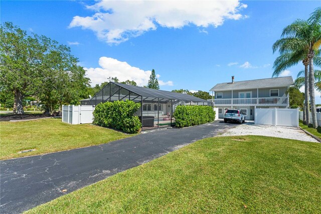 view of front of property with glass enclosure, a front lawn, fence, and driveway