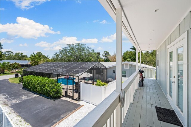 wooden deck featuring glass enclosure, an outdoor pool, and a patio