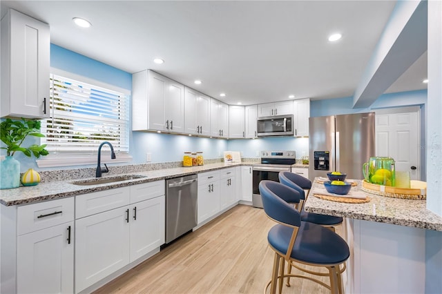 kitchen featuring light stone counters, a sink, white cabinetry, appliances with stainless steel finishes, and a kitchen bar