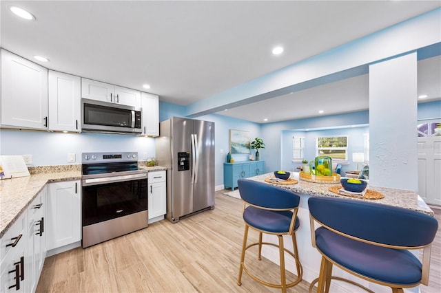 kitchen with light stone countertops, stainless steel appliances, light wood-type flooring, white cabinetry, and recessed lighting