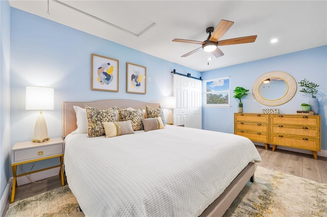 bedroom featuring light wood finished floors, a closet, a barn door, ceiling fan, and baseboards