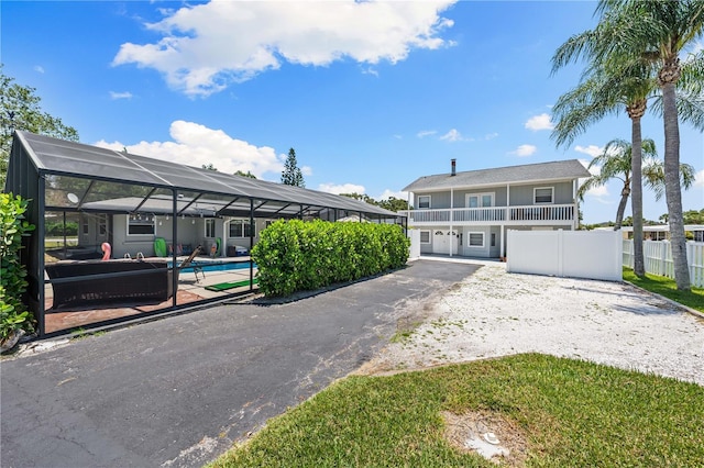 view of front of home with a lanai, a balcony, fence, an outdoor pool, and a patio area