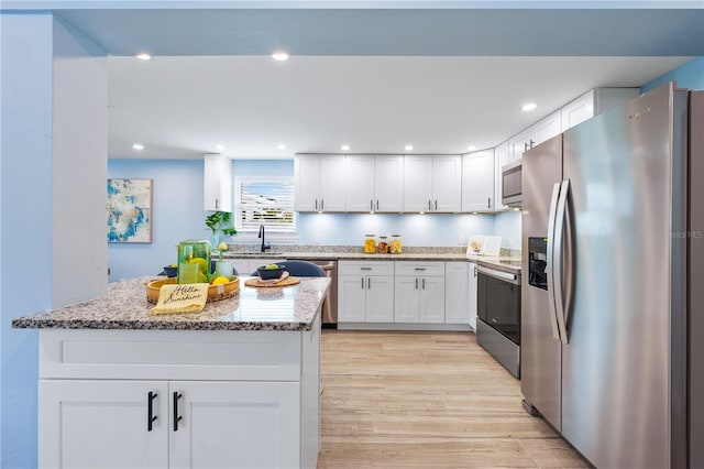 kitchen with white cabinets, light wood-style flooring, appliances with stainless steel finishes, light stone countertops, and recessed lighting