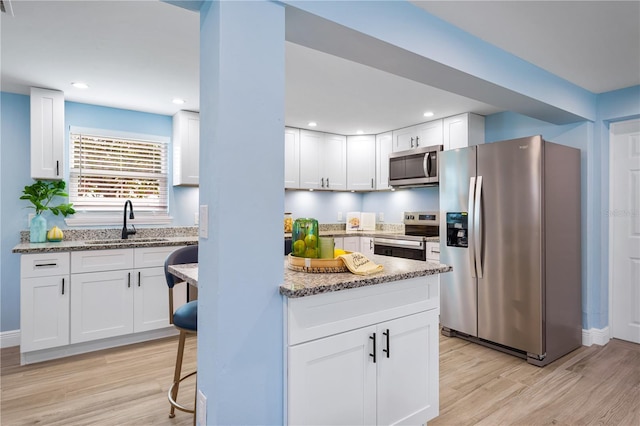 kitchen with stainless steel appliances, white cabinetry, a sink, and light stone counters