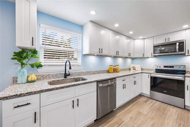 kitchen featuring appliances with stainless steel finishes, light wood-style floors, white cabinets, and a sink