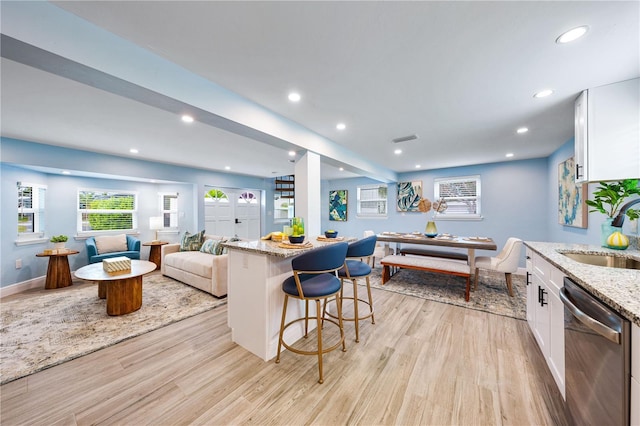 kitchen with open floor plan, white cabinets, a sink, light stone countertops, and dishwasher