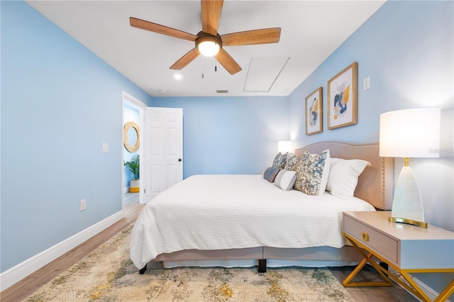 bedroom featuring wood finished floors, visible vents, a ceiling fan, baseboards, and attic access