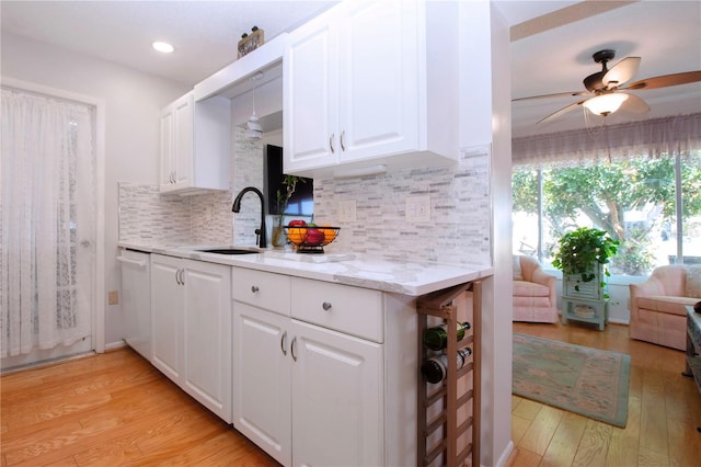 kitchen with white cabinets, light wood-type flooring, sink, and tasteful backsplash