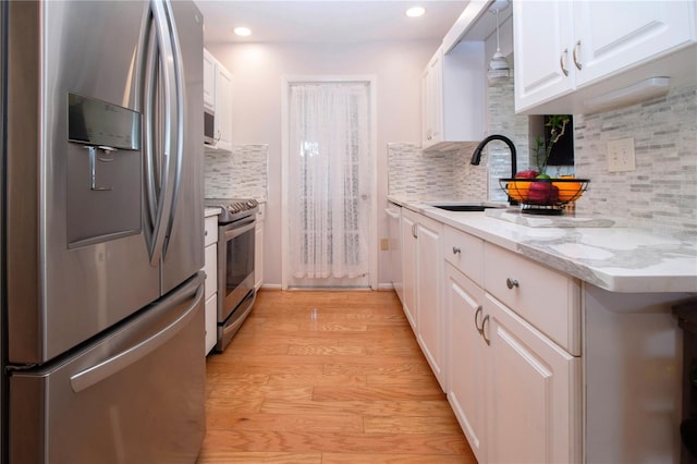 kitchen featuring light stone countertops, white cabinetry, decorative backsplash, appliances with stainless steel finishes, and light wood-type flooring