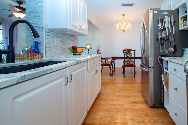 kitchen featuring white cabinets, light hardwood / wood-style floors, backsplash, and stainless steel refrigerator