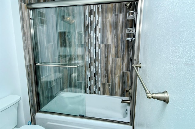 bathroom with combined bath / shower with glass door and toilet