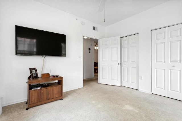 bedroom with two closets, ceiling fan, and light carpet