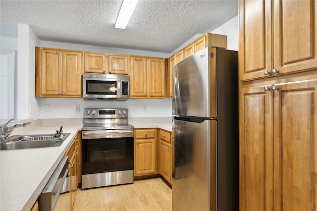 kitchen featuring stainless steel appliances, sink, light hardwood / wood-style floors, and a textured ceiling