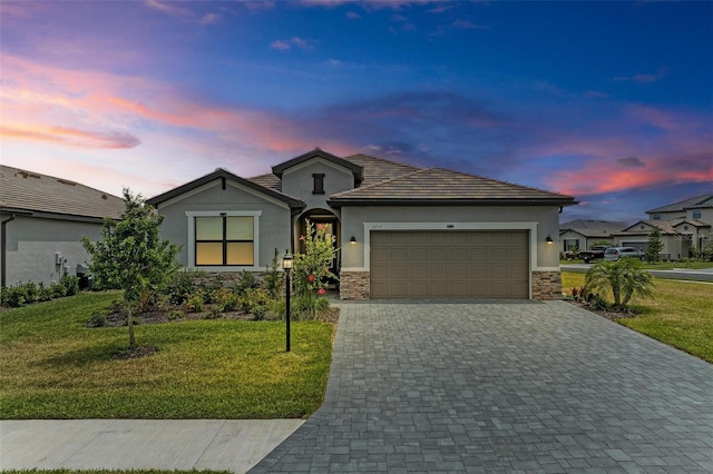 ranch-style house with an attached garage, stone siding, decorative driveway, and a lawn