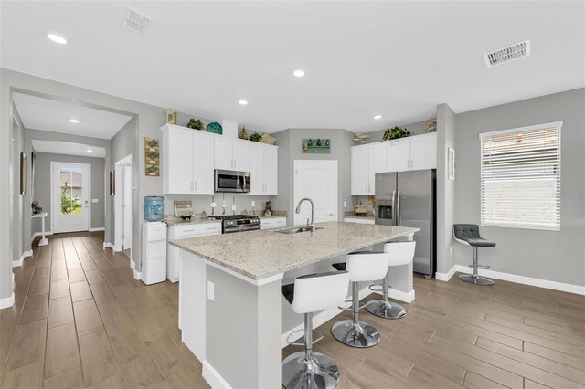 kitchen with a center island with sink, appliances with stainless steel finishes, white cabinetry, and sink