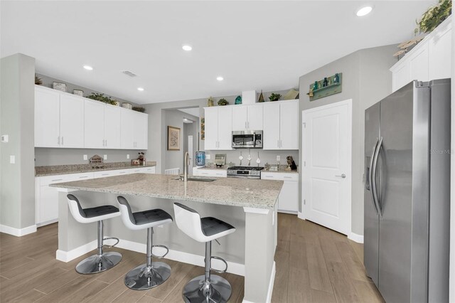 kitchen with appliances with stainless steel finishes, white cabinets, sink, wood-type flooring, and a kitchen island with sink