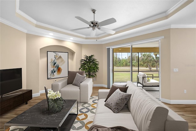 living room with light hardwood / wood-style floors, crown molding, a raised ceiling, and ceiling fan