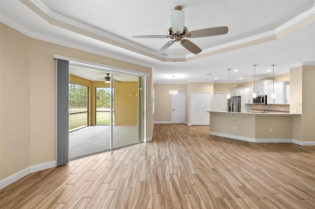 unfurnished living room with ceiling fan with notable chandelier, crown molding, a raised ceiling, and light wood-type flooring