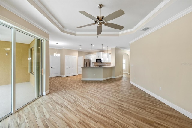 unfurnished living room with ceiling fan with notable chandelier, crown molding, a raised ceiling, and light wood-type flooring