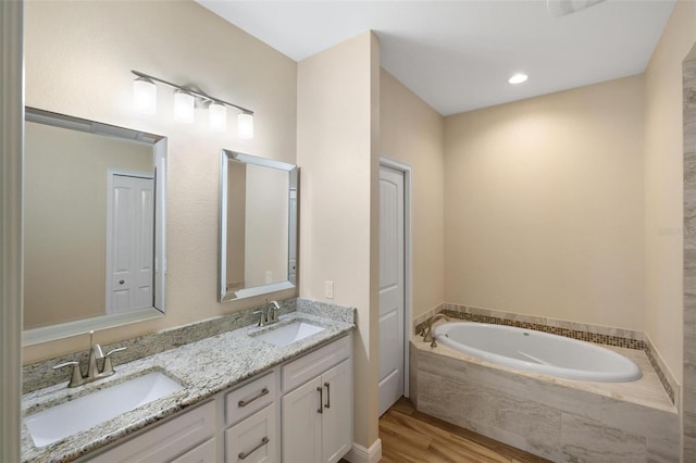 bathroom featuring vanity, hardwood / wood-style floors, and a relaxing tiled tub