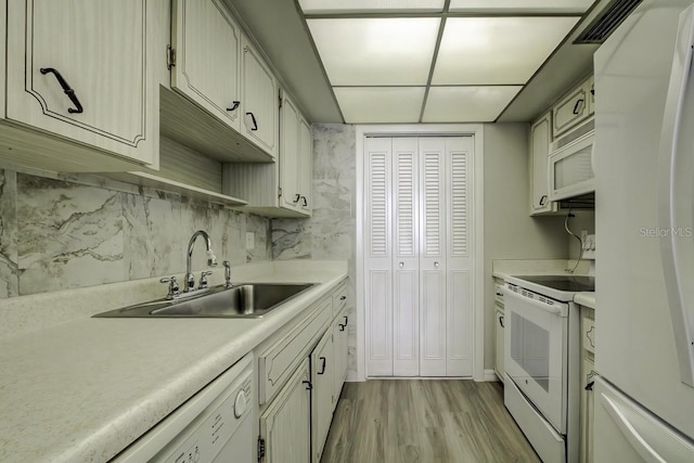 kitchen with a sink, white appliances, light wood finished floors, and light countertops