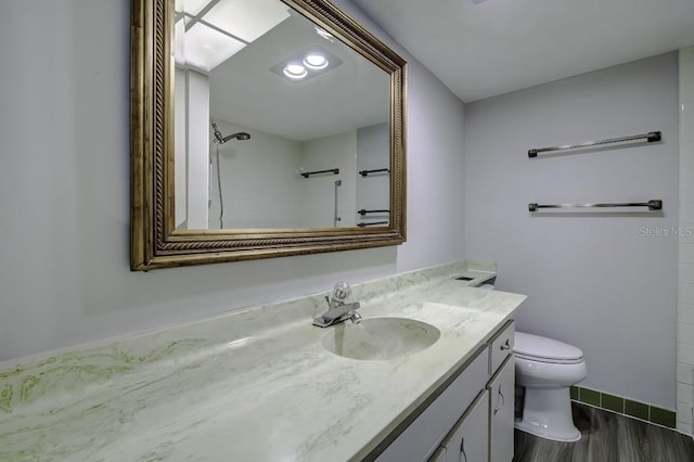 full bath featuring vanity, wood finished floors, baseboards, walk in shower, and toilet