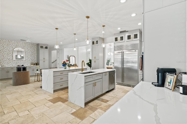 kitchen with a kitchen island with sink, sink, decorative backsplash, appliances with stainless steel finishes, and decorative light fixtures