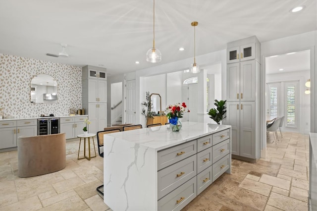 kitchen featuring wine cooler, light stone counters, a kitchen bar, gray cabinets, and a center island with sink