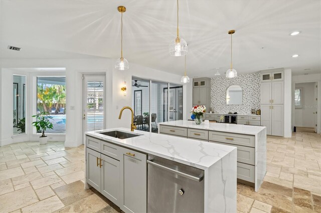 kitchen featuring pendant lighting, sink, an island with sink, tasteful backsplash, and light stone counters