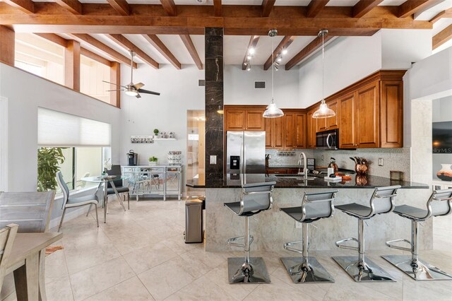 kitchen featuring pendant lighting, a towering ceiling, beamed ceiling, a breakfast bar area, and stainless steel appliances