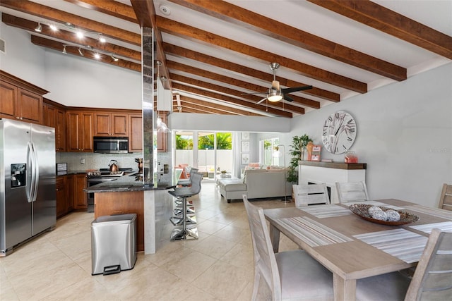 kitchen featuring appliances with stainless steel finishes, dark stone counters, backsplash, a breakfast bar, and beam ceiling