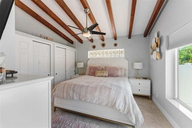 bedroom featuring ceiling fan, vaulted ceiling with beams, and two closets