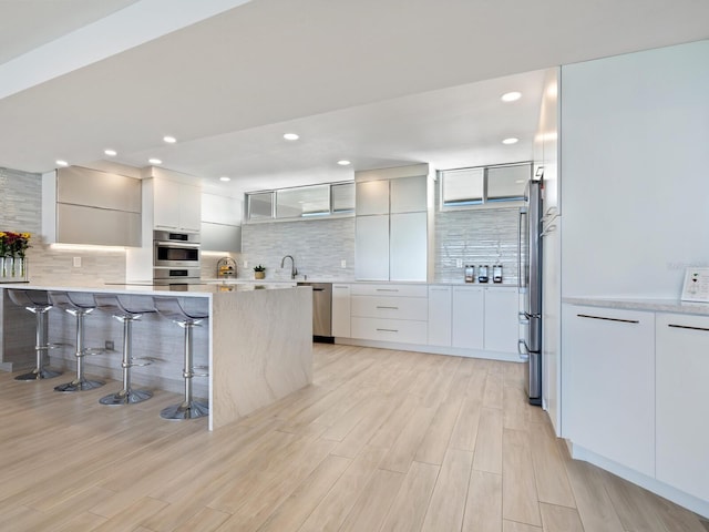 kitchen featuring decorative backsplash, stainless steel appliances, white cabinetry, and a breakfast bar area