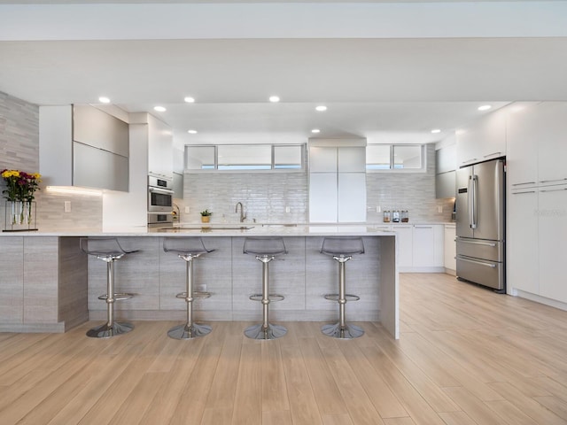 kitchen featuring white cabinetry, a kitchen breakfast bar, decorative backsplash, appliances with stainless steel finishes, and light wood-type flooring