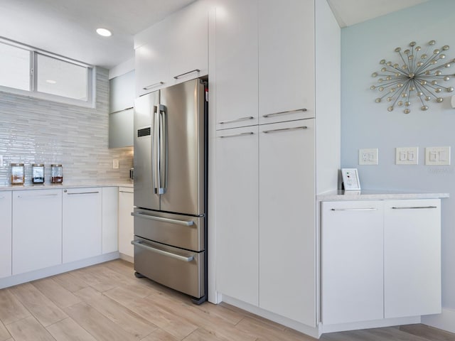 kitchen with decorative backsplash, stainless steel fridge, light hardwood / wood-style floors, and white cabinetry