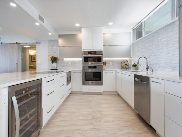 kitchen with a barn door, tasteful backsplash, white cabinetry, stainless steel appliances, and beverage cooler