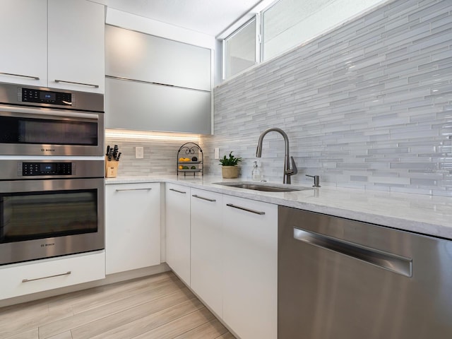 kitchen featuring sink, decorative backsplash, appliances with stainless steel finishes, light stone counters, and white cabinetry