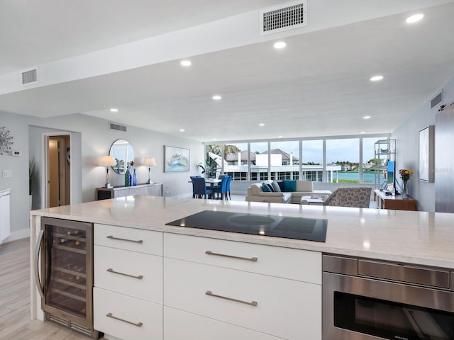 kitchen featuring light stone countertops, black electric cooktop, beverage cooler, light hardwood / wood-style floors, and white cabinetry