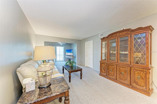 living room with light carpet, ceiling fan, and a textured ceiling