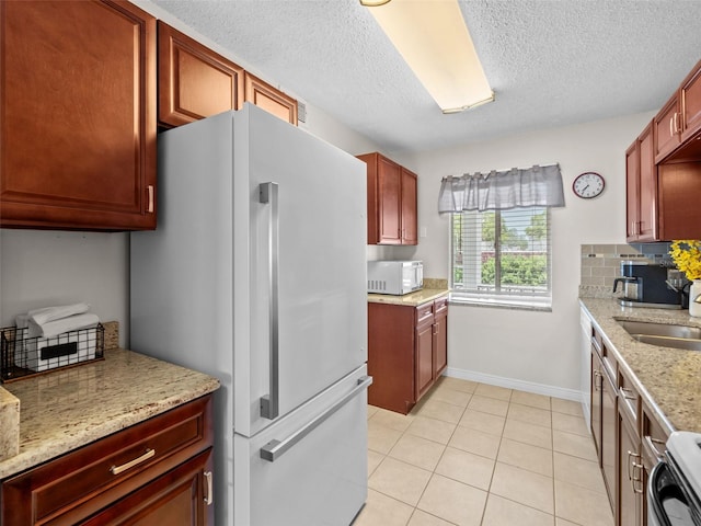 kitchen featuring white appliances, a textured ceiling, light stone counters, sink, and light tile floors