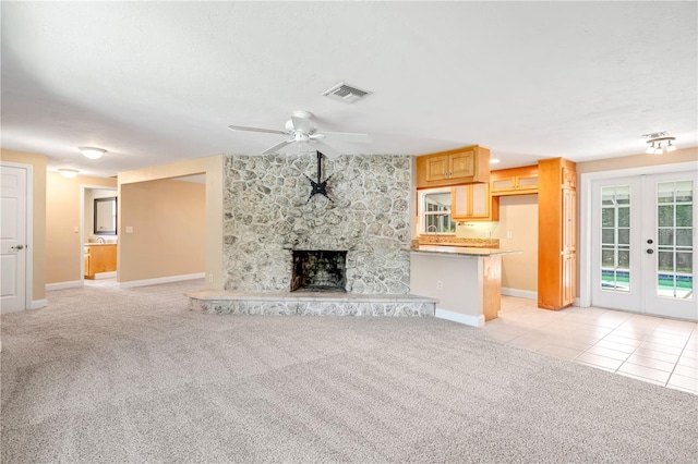 unfurnished living room featuring light carpet, french doors, ceiling fan, and a stone fireplace