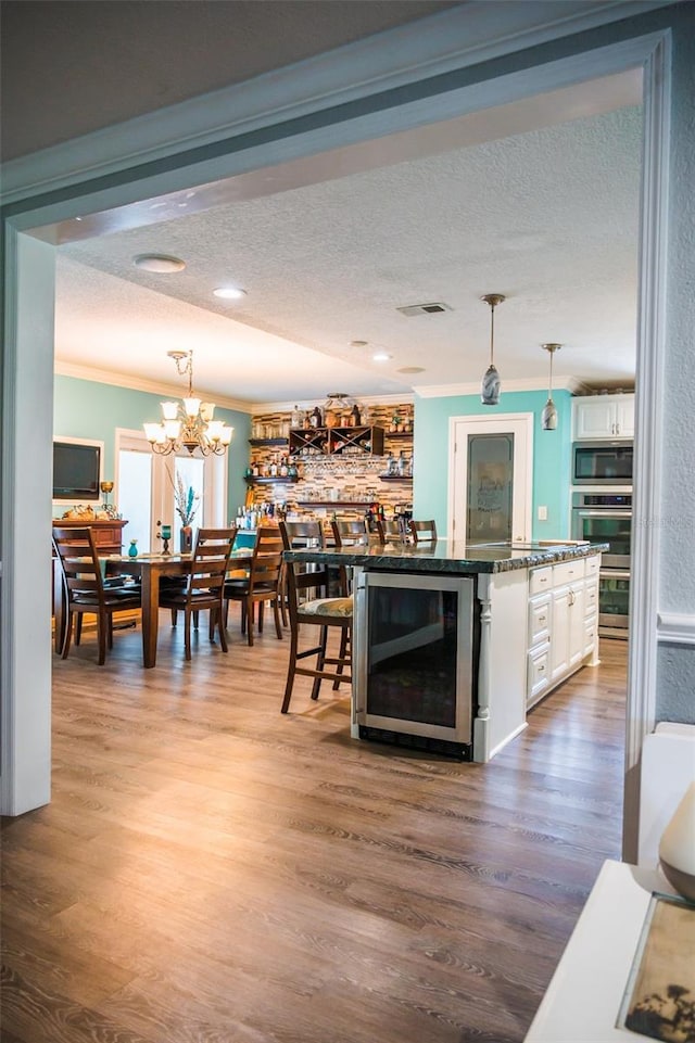 living room featuring wood-type flooring, beverage cooler, crown molding, an inviting chandelier, and a textured ceiling