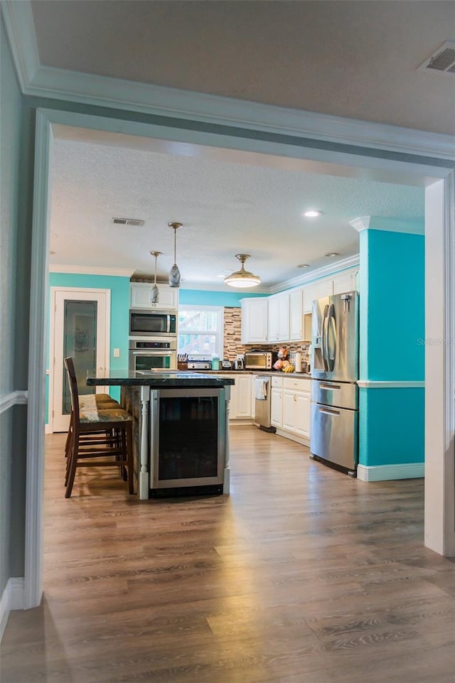 kitchen with hanging light fixtures, white cabinetry, ornamental molding, stainless steel appliances, and hardwood / wood-style flooring