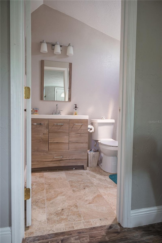 bathroom with a textured ceiling, wood-type flooring, toilet, vaulted ceiling, and vanity