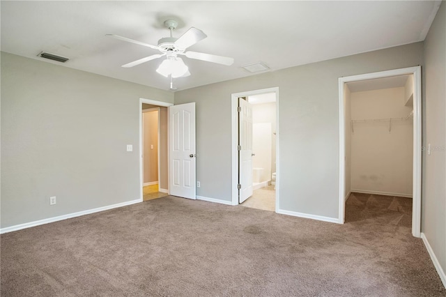 unfurnished bedroom featuring ceiling fan, ensuite bathroom, a walk in closet, light carpet, and a closet