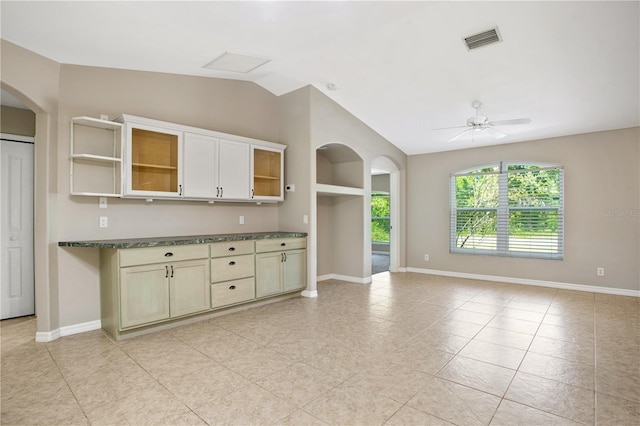 kitchen featuring light tile patterned flooring, lofted ceiling, dark stone countertops, cream cabinets, and ceiling fan